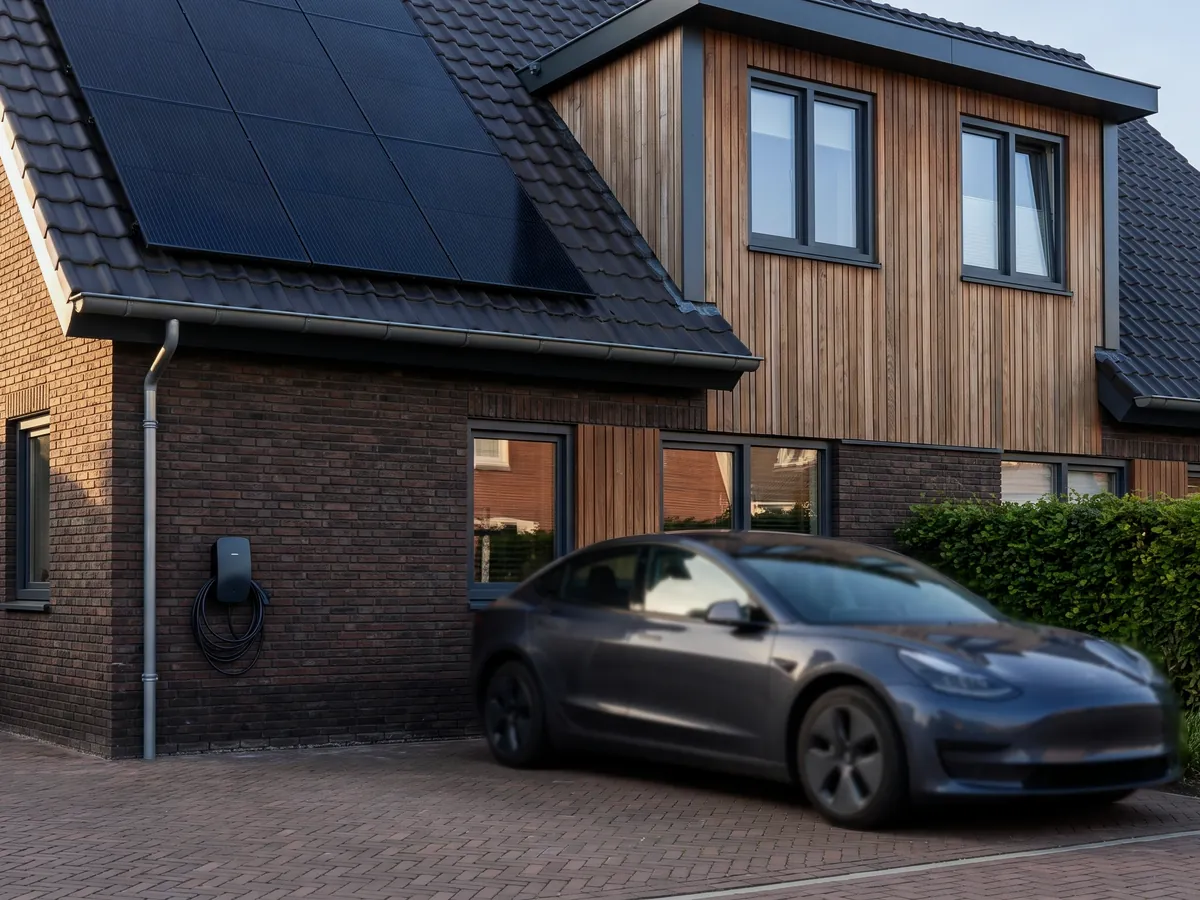 Elektrische auto op de oprit van een woning met zonnepanelen en een laadpaal aan de gevel